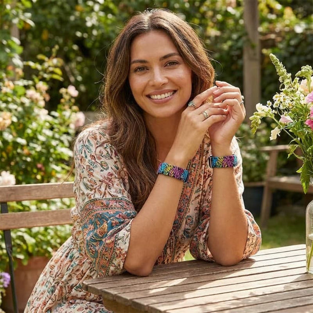 Woman wearing designer motion sickness bracelets sitting at a wooden table outdoors with flowers and greenery in the background